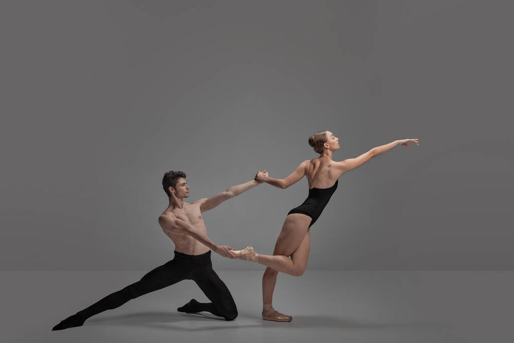 Mladý muž a žena, baletní tanečníci vystupující izolovaně přes tmavě šedé pozadí studia. Zmatená pozice. Koncept klasické taneční estetiky, choreografie, umění, krásy. Kopírovat prostor pro inzerci - Fotografie, Obrázek