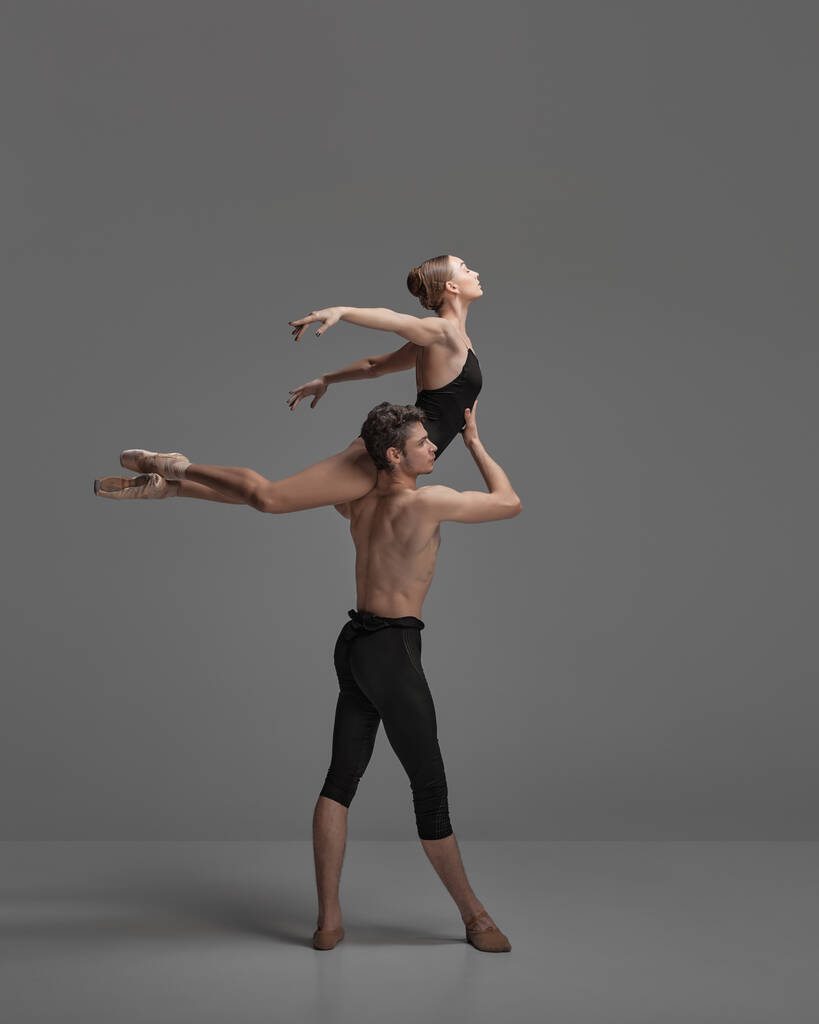 Young man and woman, ballet dancers performing isolated over dark grey studio background. Flying on a shoulder. Concept of classical dance aesthetics, choreography, art, beauty. Copy space for ad - Photo, Image