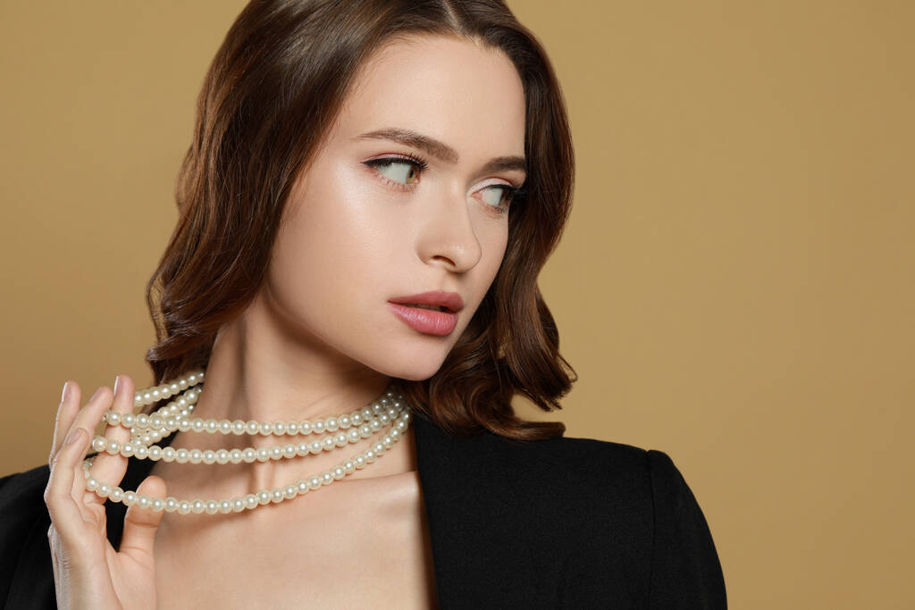 Jeune femme avec élégant collier de perles sur fond brun, espace pour le texte - Photo, image