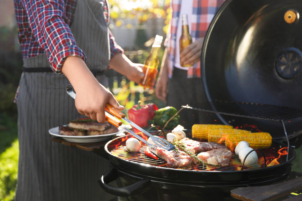 Man with drink cooking meat and vegetables on barbecue grill outdoors, closeup - Photo, Image