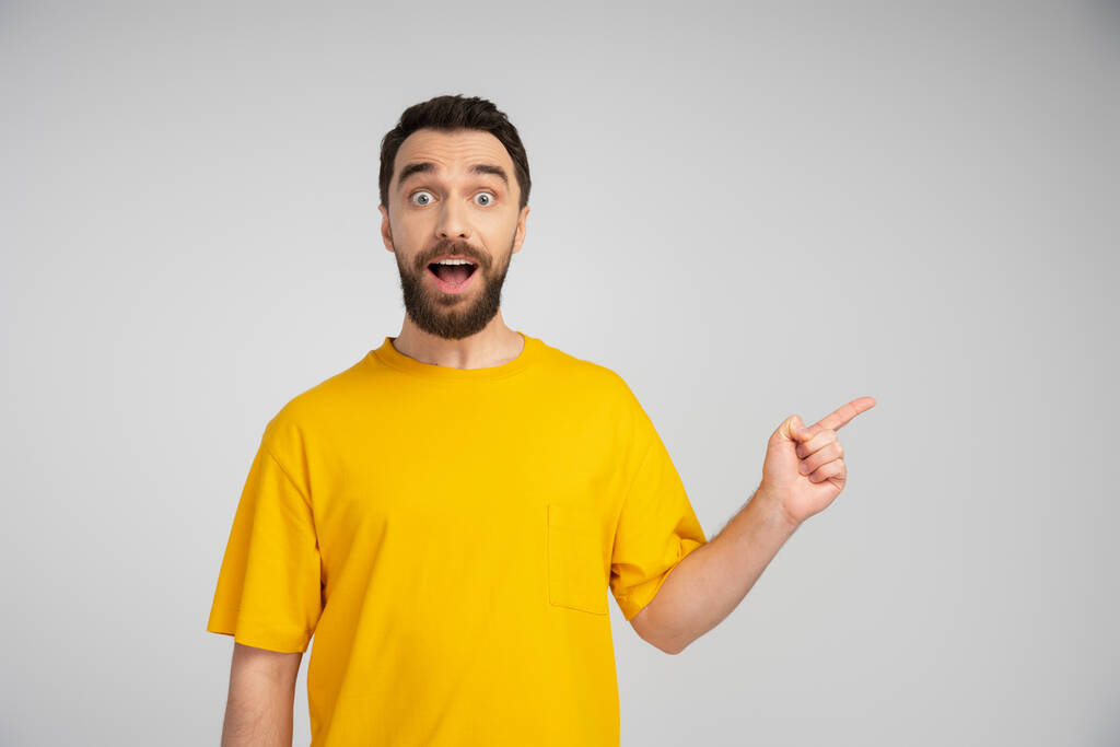 здивований чоловік у жовтій футболці дивиться на камеру і вказує пальцем ізольовано на сірому
 - Фото, зображення