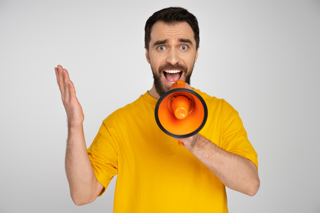 displeased man in yellow t-shirt shouting in loudspeaker isolated on grey - Photo, Image