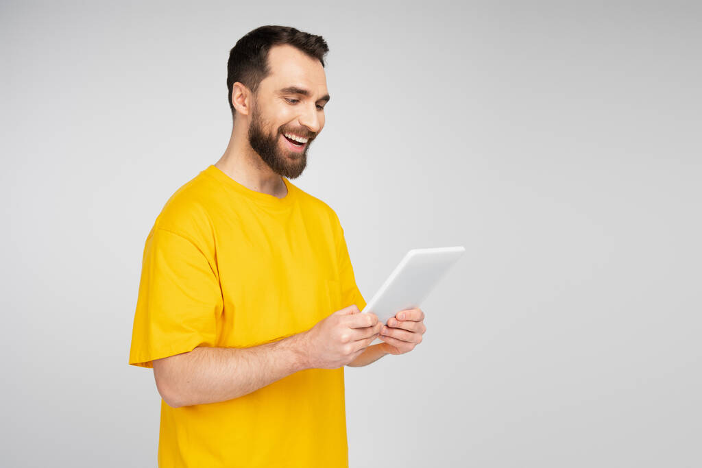 радісний бородатий чоловік дивиться на цифровий планшет ізольований на сірому
 - Фото, зображення