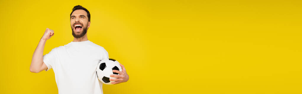 kiabáló labdarúgó rajongó labda örvendezik, és mutatja diadal gesztus elszigetelt sárga, banner - Fotó, kép