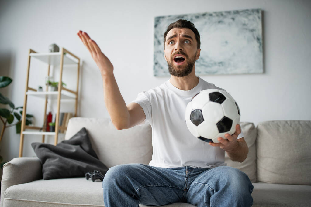 КИЕВ, УКРАИНА - 21 ОКТЯБРЯ 2022: недовольный мужчина проводит футбол и смотрит чемпионат дома - Фото, изображение