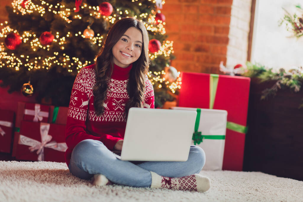 Φωτογραφία του θετικού αισιόδοξου ωραίο κορίτσι με καστανά μαλλιά φορούν κόκκινο στολίδι jumper κάθεται με φορητό υπολογιστή πληκτρολογώντας email στο σπίτι σε εσωτερικούς χώρους. - Φωτογραφία, εικόνα