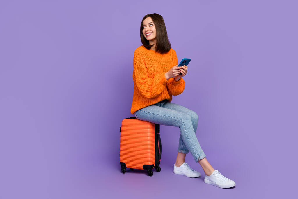 Pełny rozmiar zdjęcie cute młoda kobieta trzymać urządzenie czekać taxi nosić modne pomarańczowy dzianina odzież izolowane na fioletowy kolor tła. - Zdjęcie, obraz