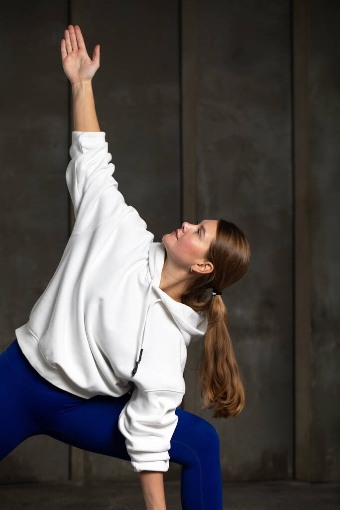 De atleet staat in de driehoek pose. Pilates en yoga training. De vrouw maakt een kanteling naar de zijkant terwijl ze staat. - Foto, afbeelding
