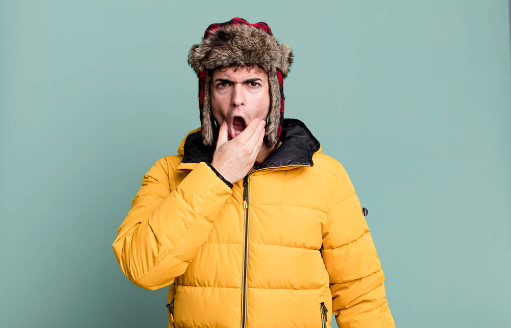 volwassen man met mond en ogen wijd open en hand op kin draagt anorak. winter- en koudeconcept - Foto, afbeelding