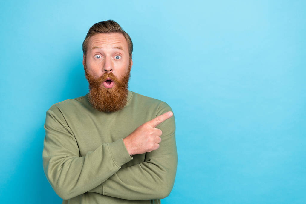 Portrait d'impressionné beau gars avec gingembre coiffure porter pullover kaki indiquant espace vide isolé sur fond de couleur turquoise. - Photo, image
