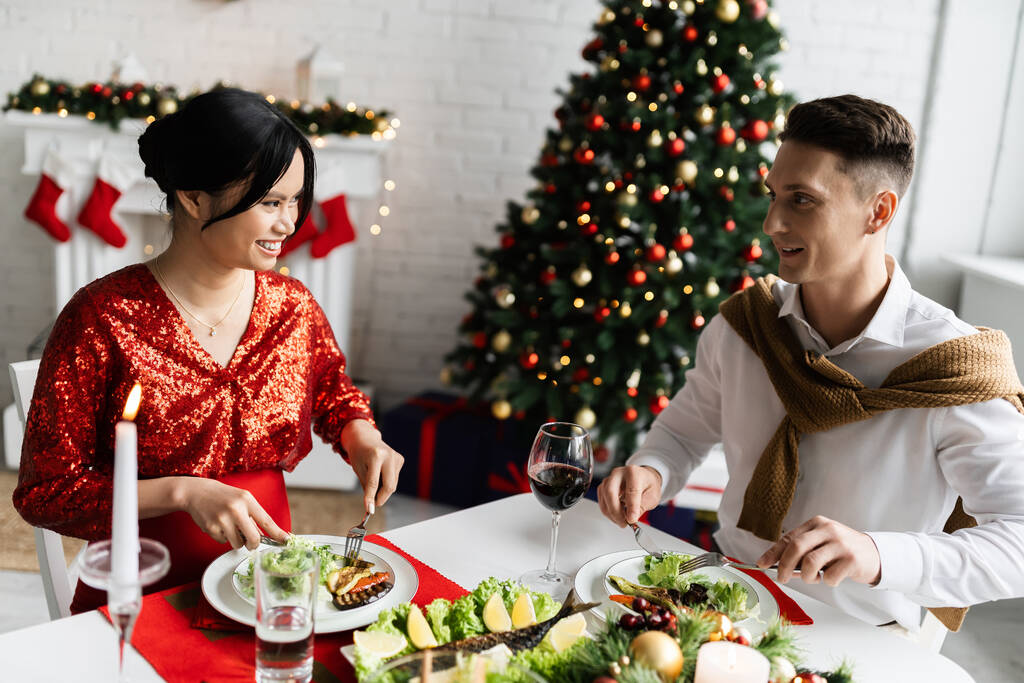 беременная азиатка улыбается счастливому мужу во время романтического рождественского ужина  - Фото, изображение
