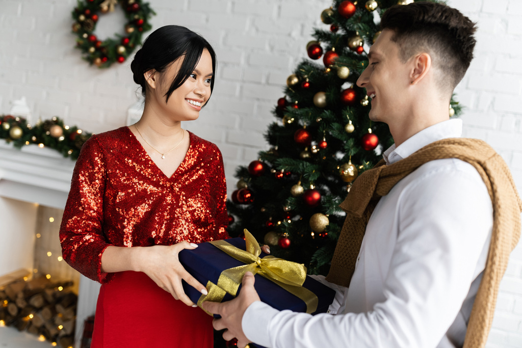 incinta e soddisfatto asiatico donna presa regalo scatola da marito vicino decorato albero di Natale  - Foto, immagini