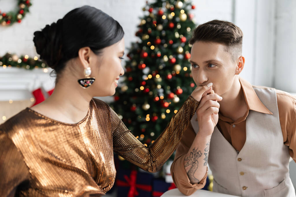 tattooed man kissing hand of smiling asian wife in elegant shiny blouse - Photo, Image