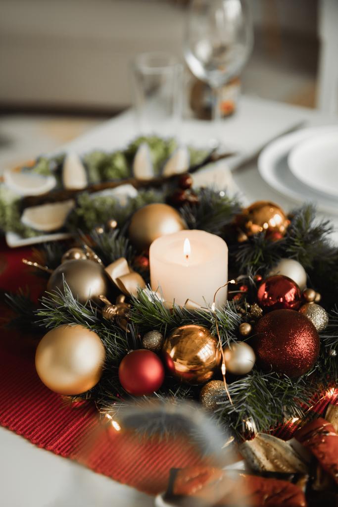 γιορτινό στεφάνι Χριστουγέννων με αναμμένο κερί και γυαλιστερά μπιχλιμπίδια στο τραπέζι σερβιρίσματος  - Φωτογραφία, εικόνα