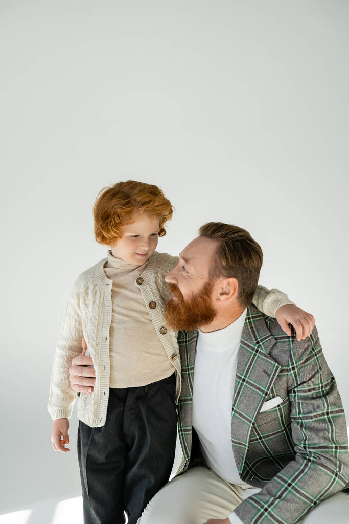 Pozitivní muž v kostkované bundě objímání ryšavý syn na šedém pozadí - Fotografie, Obrázek
