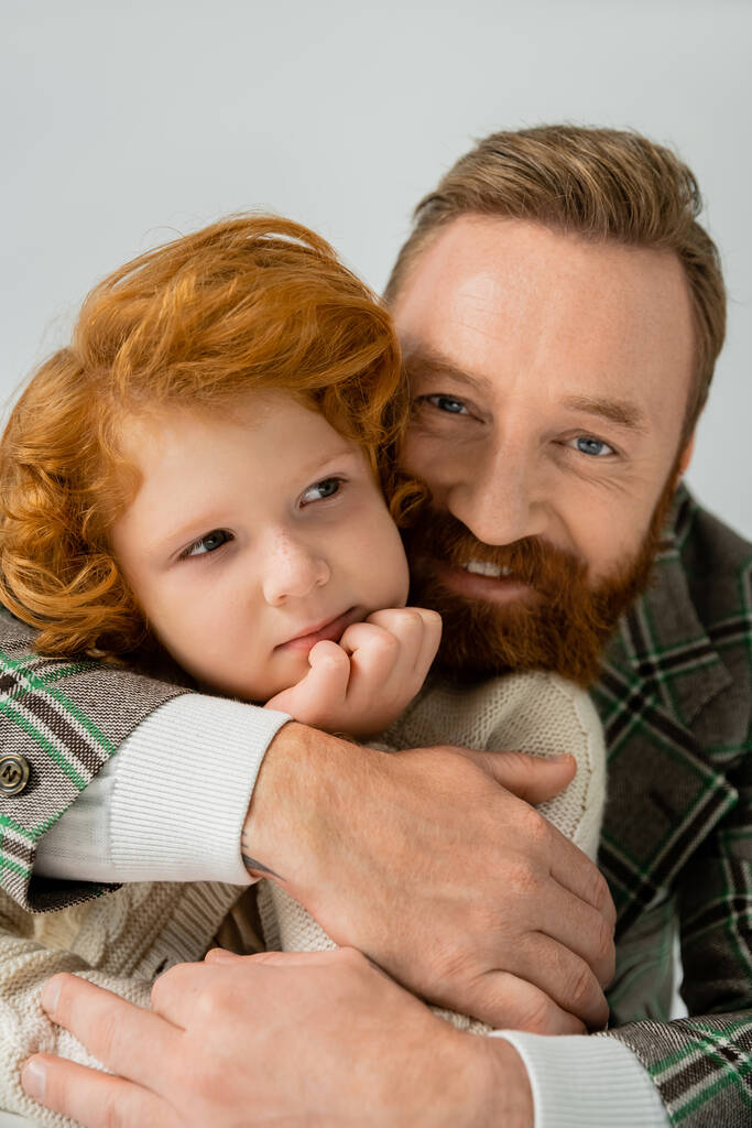 Szakállas férfi ölelkezik vörös hajú és szeplős fia elszigetelt a szürke  - Fotó, kép