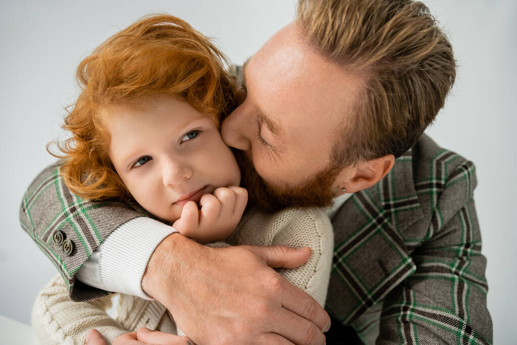 Бородатий батько цілує червоного волохатого сина в бежевому джемпері ізольовано на сірому
  - Фото, зображення