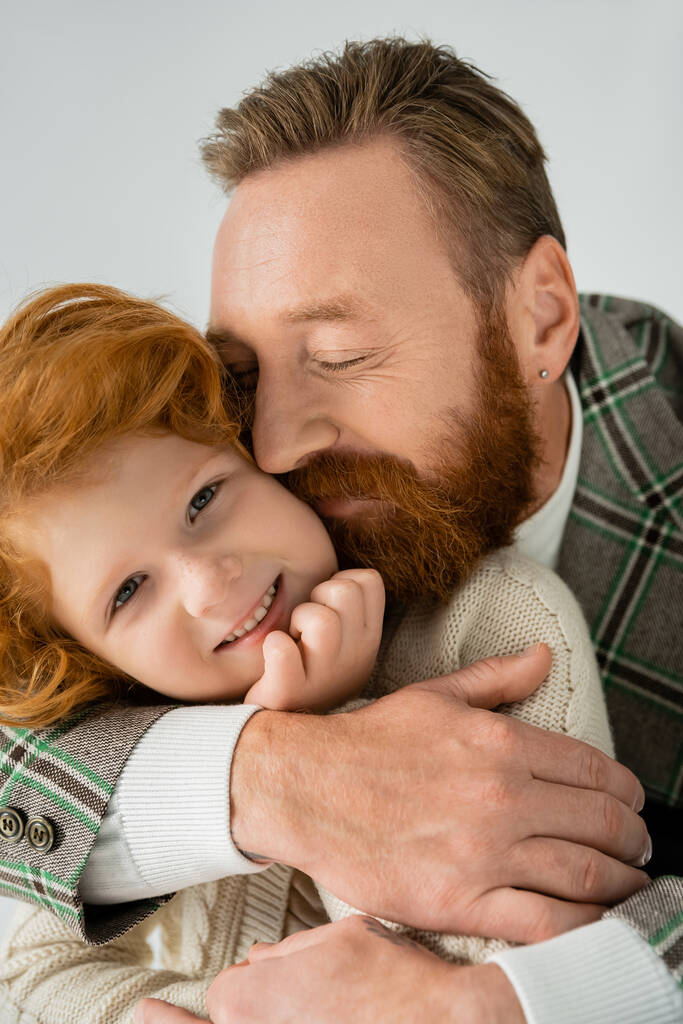 Homem satisfeito e barbudo abraçando o filho ruivo isolado no cinza  - Foto, Imagem