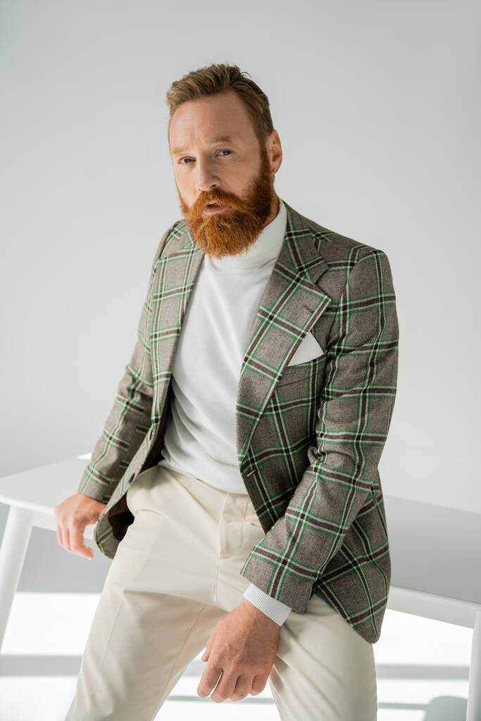 Uomo alla moda in giacca posa vicino al tavolo su sfondo grigio con luce solare  - Foto, immagini