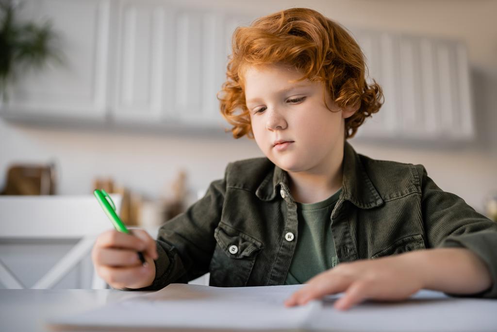 Peniksen punapää poika tilalla kynä tehdessään läksyjä lähellä hämärtynyt muistikirja - Valokuva, kuva