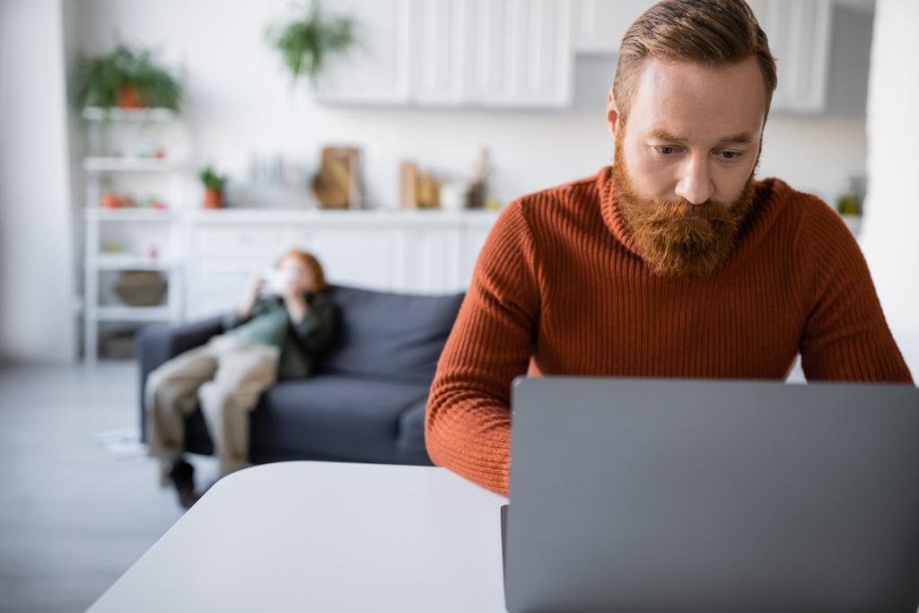 redhead and bearded man working on laptop near son on blurred background - Photo, Image