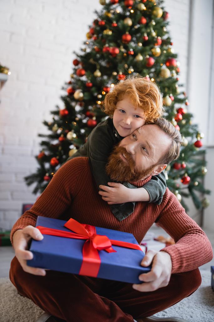 赤毛子供抱擁幸せなひげを生やしたお父さん座って床にクリスマスプレゼント - 写真・画像
