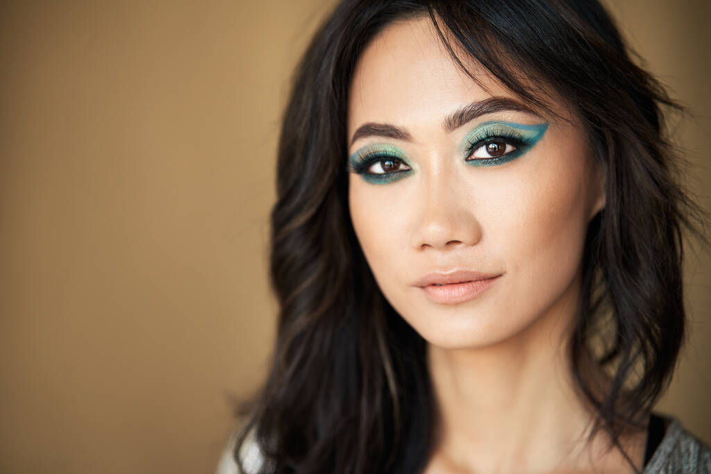 Ritratto di bella ragazza asiatica modello con i capelli lunghi e trucco luminoso su sfondo beige primo piano - Foto, immagini