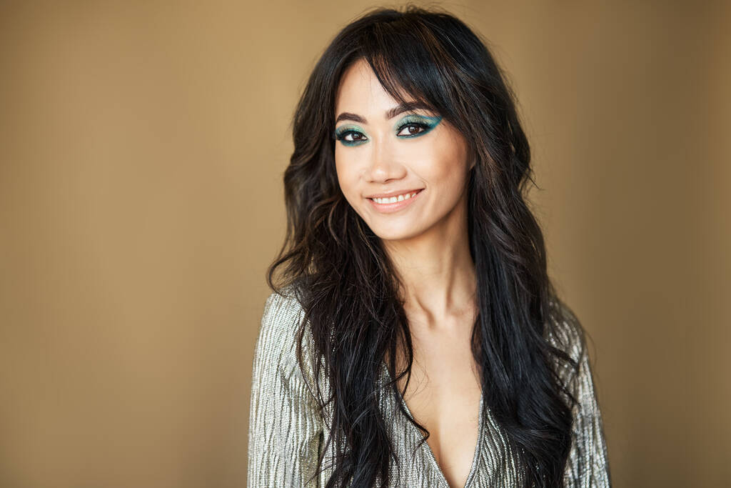 Joli portrait de femme souriante. Beau modèle asiatique avec un maquillage lumineux et les cheveux longs posant en regardant la caméra sur fond beige - Photo, image