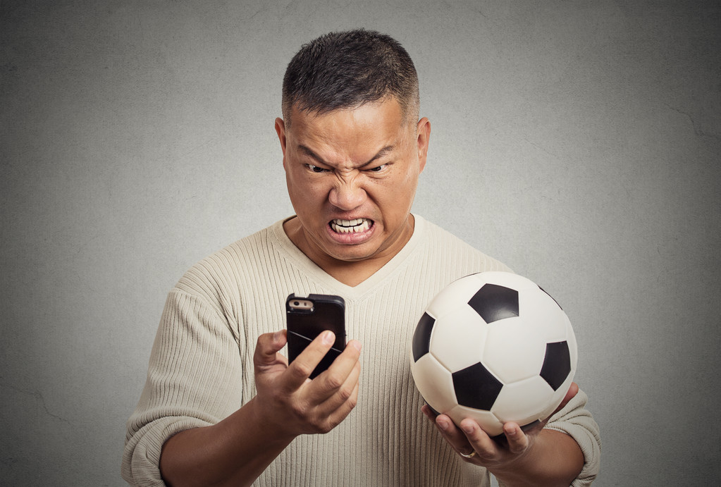 携帯電話のセルのスマートを探している欲求不満の男ゲーム開催サッカーを見て  - 写真・画像