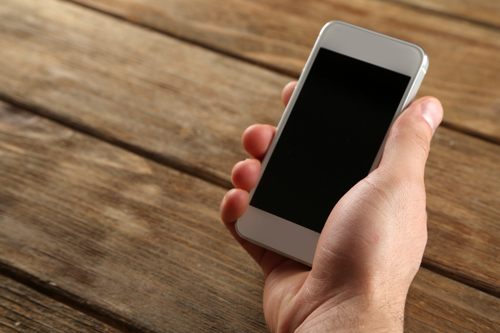 Mão segurando telefone celular inteligente no fundo da mesa de madeira
 - Foto, Imagem