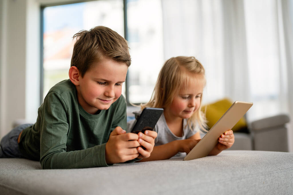 Kislány és fiú néz videó vagy játék a digitális eszköz táblagép, okostelefon. A gyermekek digitális függőségének fogalma. - Fotó, kép