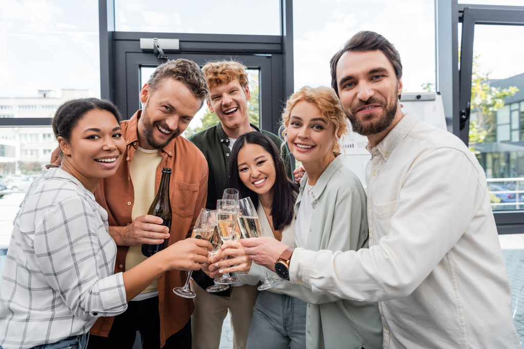 multi-etnische zakelijke collega 's glimlachen op de camera en klinkende champagne glazen op corporate party - Foto, afbeelding