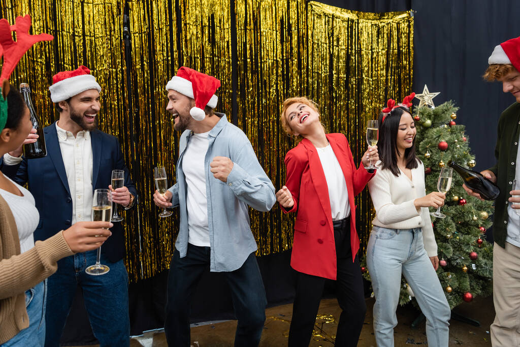 Multiethnische Geschäftsleute tanzen bei Weihnachtsfeier im Büro mit Champagner  - Foto, Bild