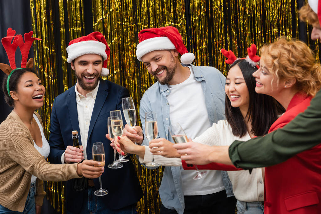 Pozytywne międzyrasowych ludzi biznesu trzymających szampana podczas świątecznej imprezy korporacyjnej w biurze  - Zdjęcie, obraz