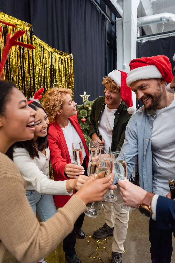 Többnemzetiségű üzletemberek mikulás sapkában pezsgőt tartanak, miközben ünneplik a karácsonyt az irodában.  - Fotó, kép