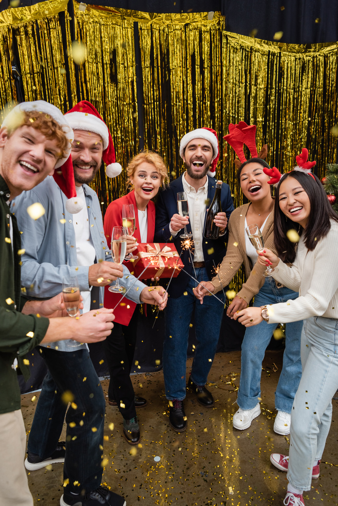 Міжрасові ділові люди тримають блискітки і шампанське під конфетті під час корпоративної вечірки в офісі
  - Фото, зображення