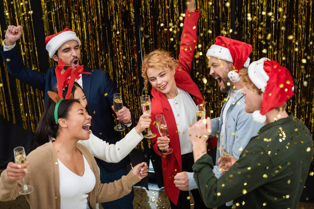 Vista de alto ângulo de negócios multiétnicos com champanhe dançando perto de confete e ouropel durante festa corporativa no escritório  - Foto, Imagem