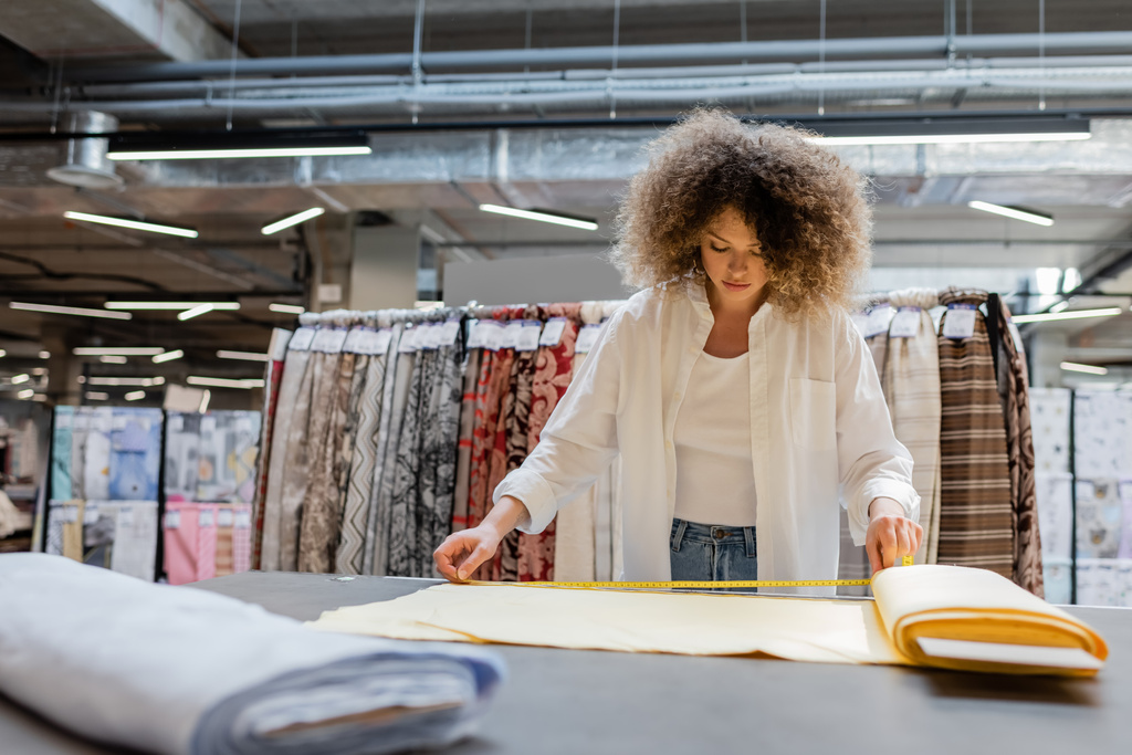 Lockige Verkäuferin misst gelbe Stoffrolle im Textilgeschäft  - Foto, Bild