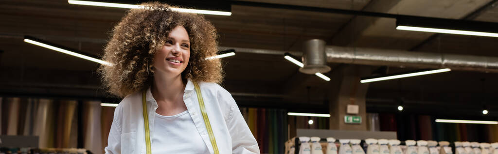 vendeuse joyeuse avec les cheveux bouclés debout dans la boutique de textile, bannière - Photo, image