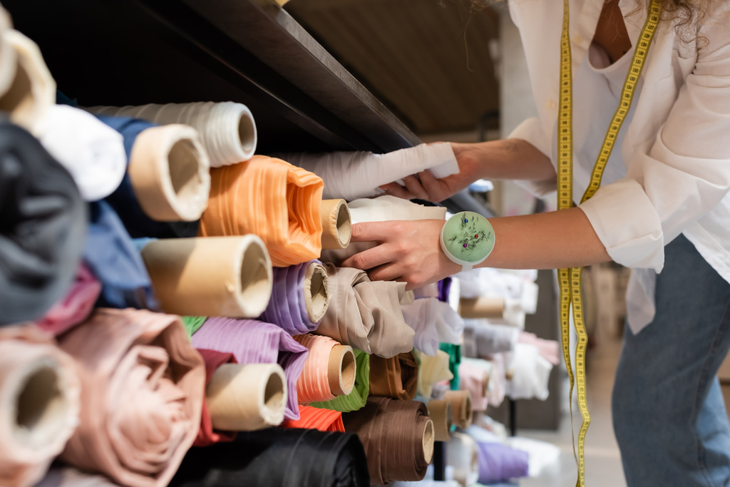 oříznutý pohled prodavačky na výběr mezi barevnými látkovými rolkami na policích textilního obchodu - Fotografie, Obrázek