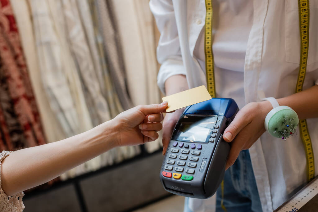 Ausgeschnittene Ansicht einer Verkäuferin mit Kreditkartenlesegerät in der Nähe eines Kunden in einem Textilgeschäft - Foto, Bild