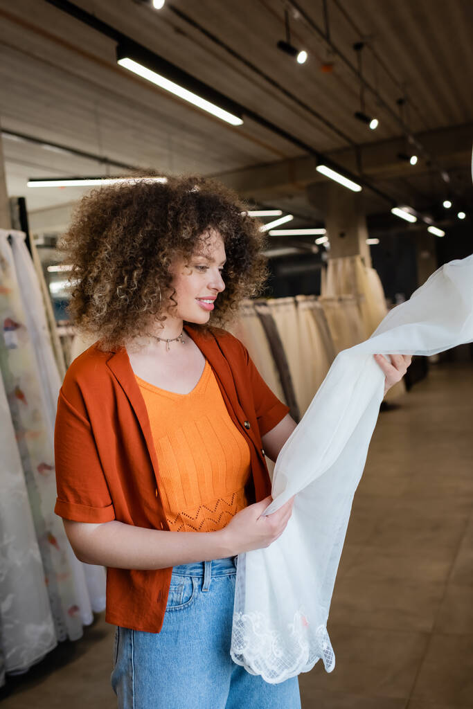 Positieve vrouw kijkt naar gordijnen in wazig textiel winkel  - Foto, afbeelding