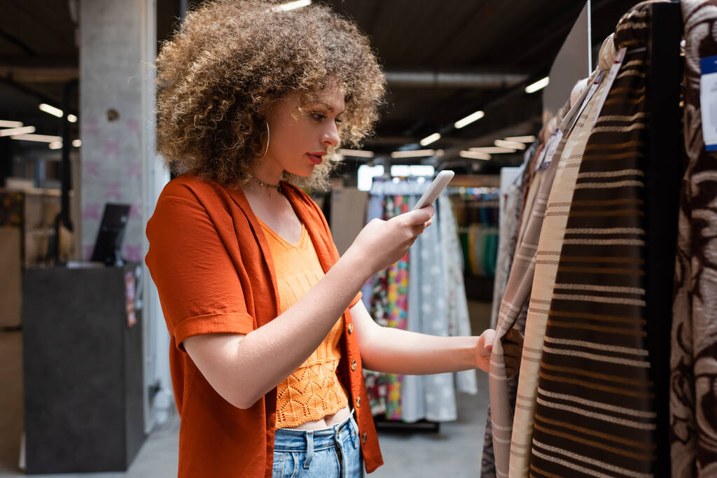 Curly zákazník fotografování na mobilu při výběru tkaniny v textilním obchodě  - Fotografie, Obrázek