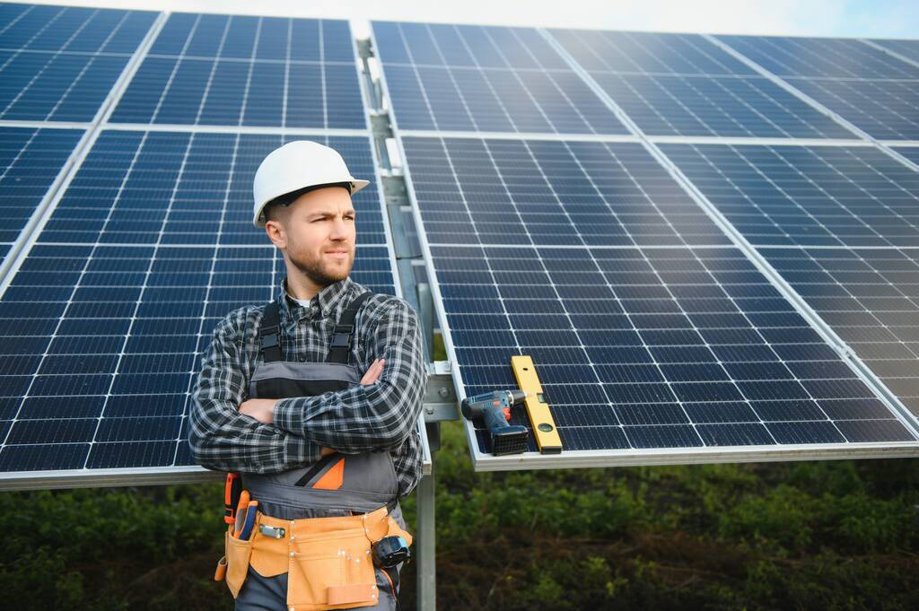 Profesionální pracovník, který instaluje solární panely na kovovou konstrukci, používá různé vybavení, nosí helmu. Inovativní řešení pro energetické řešení. Používejte obnovitelné zdroje. Zelená energie - Fotografie, Obrázek