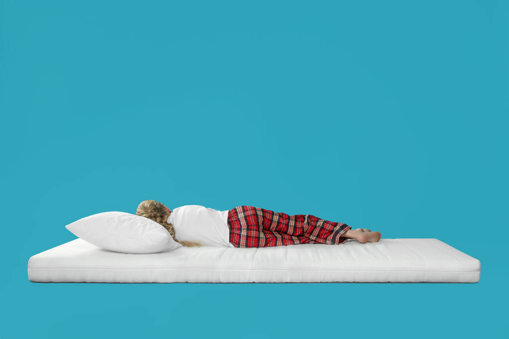 Mała dziewczynka śpi na wygodnym materacu na jasnoniebieskim tle, miejsce na tekst - Zdjęcie, obraz