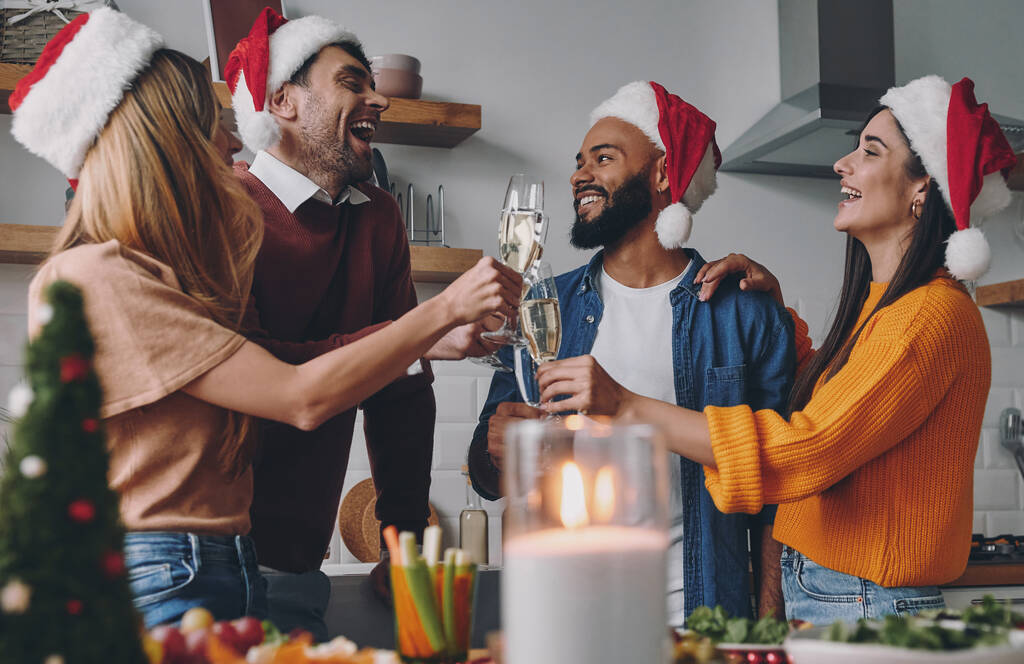 Neşeli gençler evde Noel yemeğinin tadını çıkarırken şampanyayla kadeh kaldırıyorlar. - Fotoğraf, Görsel