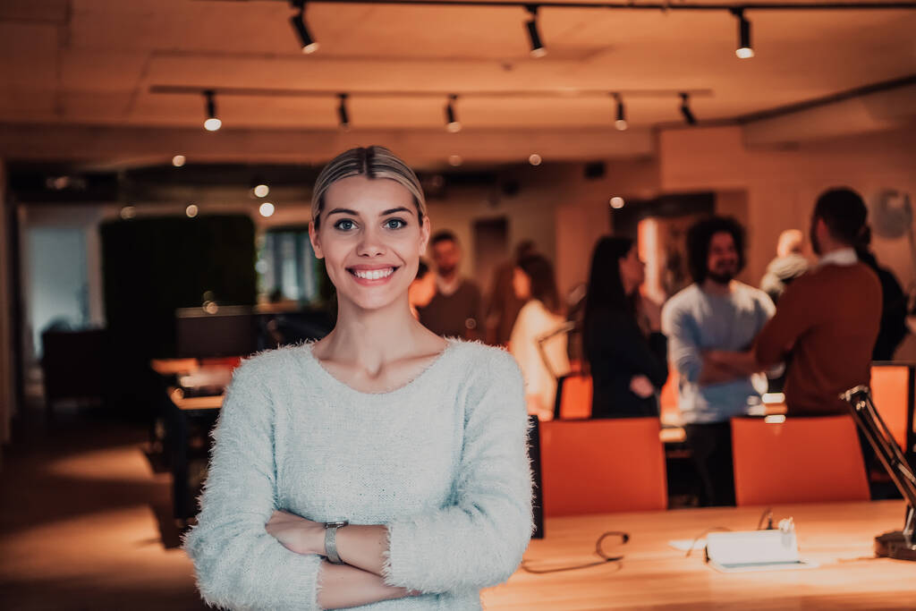 Portretfoto van een moderne blonde op een pauze van het werk in een modern kantoor. Op de achtergrond werkt het team aan de projecten.  - Foto, afbeelding