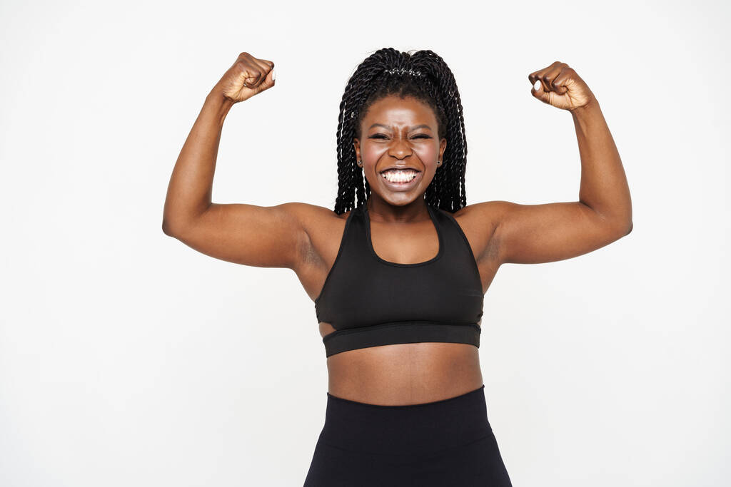 Jeune femme noire montrant ses biceps et souriant isolé sur fond blanc - Photo, image