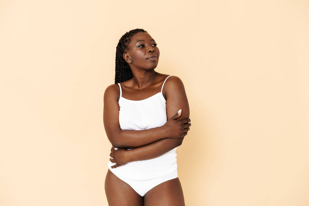 Schwarze junge Frau mit Afro-Zöpfen posiert in Unterwäsche isoliert über beigem Hintergrund - Foto, Bild