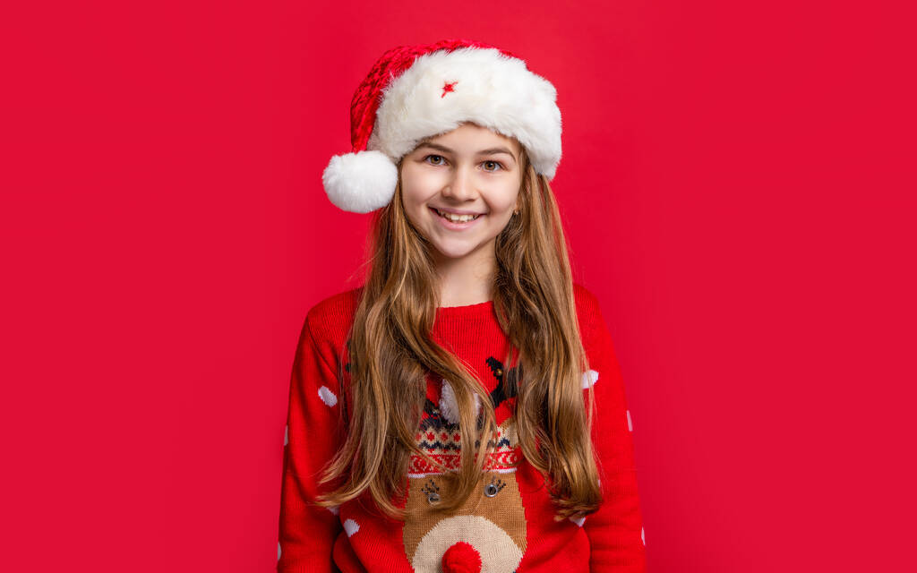 glücklich Teenager Mädchen mit Weihnachtsmann Hut auf rotem Weihnachtshintergrund. Weihnachten Teen Mädchen mit Weihnachtsmann Hut. Teenie-Mädchen tragen zu Weihnachten Pullover und Weihnachtsmütze. Frohe Weihnachten. - Foto, Bild